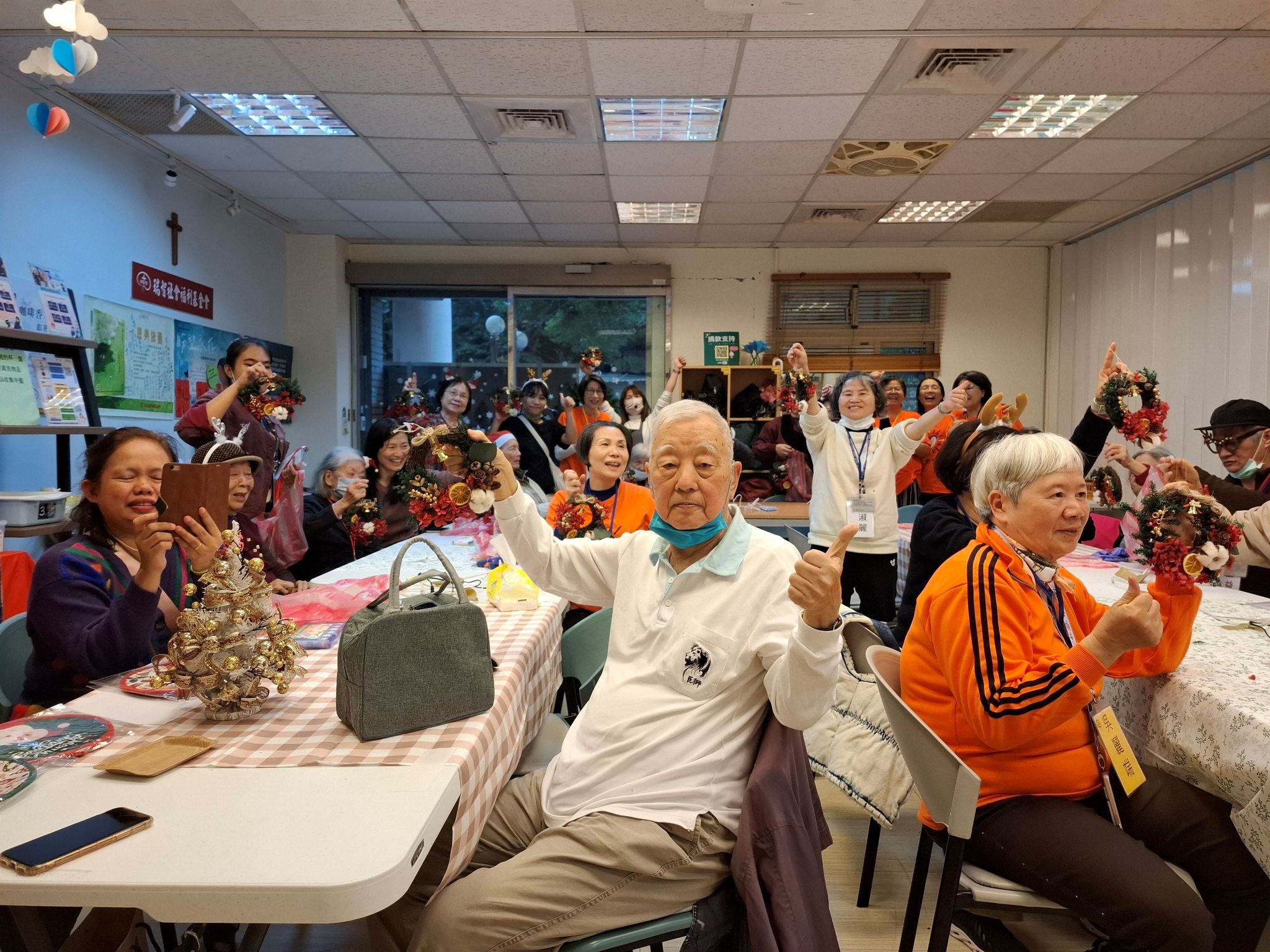 莊爺爺在甘泉咖啡坊自信地對著鏡頭比讚並展示手作花圈